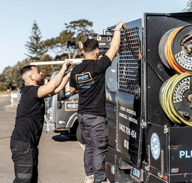 Plumbers loading equipment beside the service truck