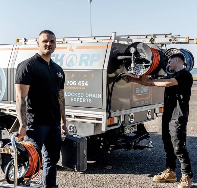 Two plumbers preparing hose reels beside their service vehicle